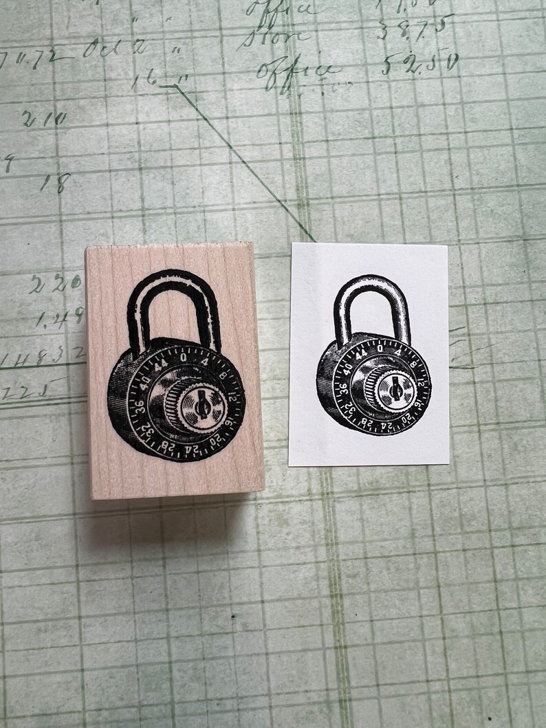 May include: A wooden rubber stamp with a black and white image of a combination padlock. The padlock has a dial with numbers from 0 to 40.