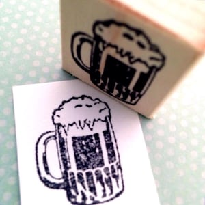 May include: A black and white illustration of a beer mug with foam on top. The mug is drawn in a simple, cartoon style.
