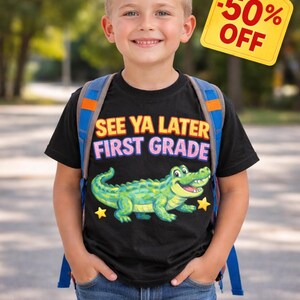 May include: A young boy wearing a black t-shirt with the text "SEE YA LATER FIRST GRADE" and a cartoon alligator graphic. He is wearing a backpack and smiling. A yellow tag reads "-50% OFF".