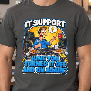 May include: A charcoal grey t-shirt featuring a cartoon graphic of a stressed IT worker with a headset and wrench, surrounded by computers, pizza boxes, and tangled cables. The text reads IT SUPPORT HAVE YOU TURNED IT OFF AND ON AGAIN?