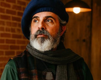 May include: A navy blue beret is worn by a person with a white beard and a gray scarf. The person is wearing a green shirt and a plaid vest. The background includes a brick wall and a warm light.