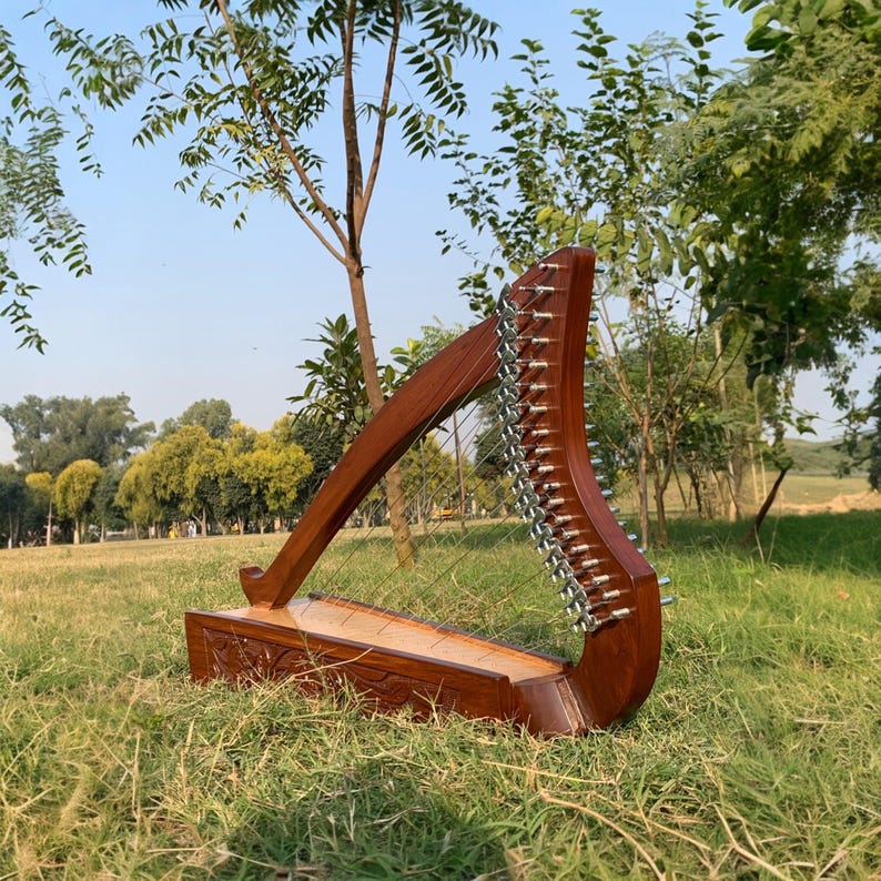 May include: A wooden harp with a dark brown finish, set outdoors on a grassy lawn. The harp has a curved soundbox and a series of strings. The harp is a musical instrument.