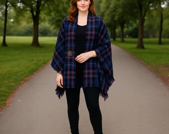 May include: A woman wearing a blue, purple, and black plaid shawl with fringe. The shawl is secured with a brown clasp. The woman is wearing a black top, black pants, and black boots. The background is a tree-lined path.