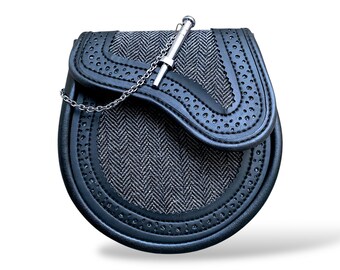 Può includere: Un sporran in pelle nera con un fronte a spina di pesce grigio. Presenta una catena d'argento e un perno decorativo in metallo. I bordi sono rifiniti con cuciture e piccoli ritagli circolari. Un accessorio scozzese tradizionale.