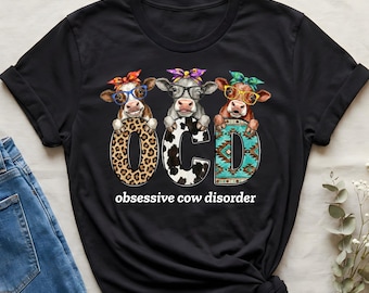 May include: Black t-shirt featuring the text "OCD obsessive cow disorder." The design includes three cartoon cows wearing glasses and bandanas, each holding a letter of the word "OCD." The "O" is leopard print, the "C" is black and white, and the "D" has a turquoise pattern.