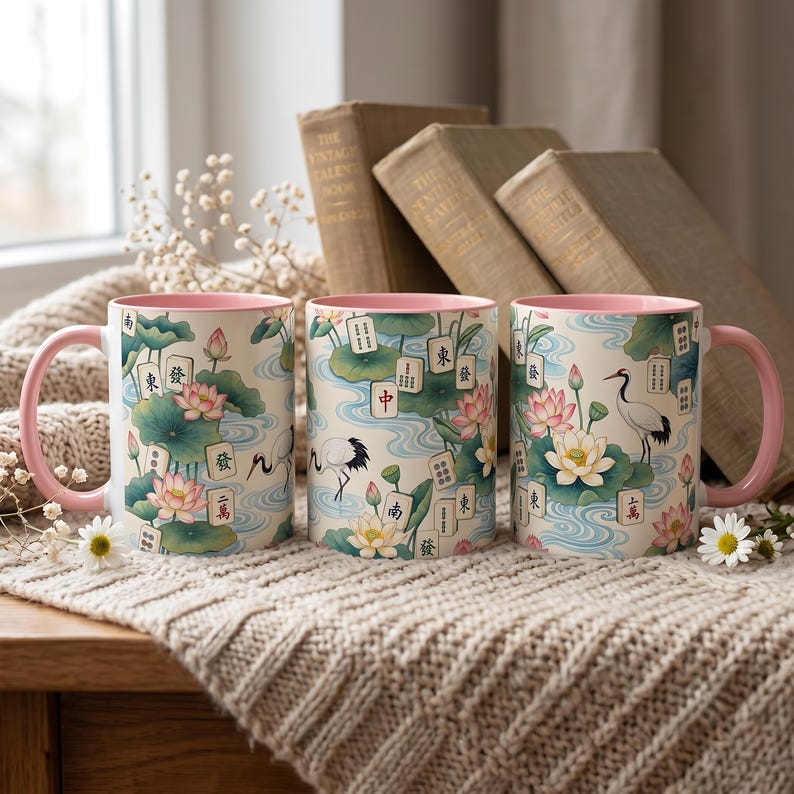 May include: Three ceramic mugs with pink handles and interiors, featuring a repeating pattern of lotus flowers, green lily pads, blue water ripples, white cranes, and mahjong tiles with various Chinese characters printed on the exterior surface.