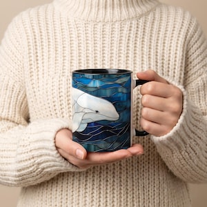 May include: A ceramic mug featuring a stained glass style illustration of a white beluga whale swimming through deep blue ocean waves. The mug has a solid black handle and a black interior rim, showcasing a detailed aquatic design.