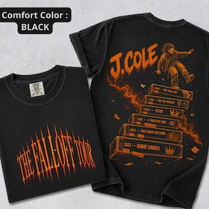 May include: A black t-shirt featuring orange graphics. The front displays the text THE FALL-OFF TOUR. The back shows a figure above a stack of labeled blocks with years and titles including 2013 BORN SINNER, 2014 FOREST HILLS DRIVE, 2016 4 YOUR EYEZ ONLY, KOD, 2021 THE OFF-SEASON, and 2024 THE FALL-OFF.