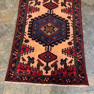 May include: A rectangular rug with a central peach field, framed by a navy blue and red border. The rug features geometric patterns in navy, red, and brown, with a central diamond-shaped design. The rug's dimensions are approximately 3 x 5 feet.