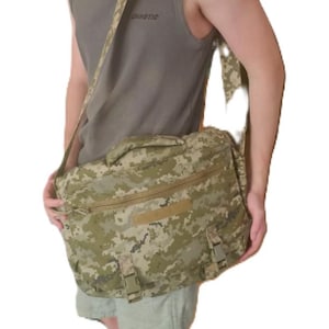 May include: A camouflage messenger bag with a shoulder strap and multiple compartments. The bag features a digital camo pattern in shades of green, tan, and brown. The bag has a handle on top and two buckle closures on the front.