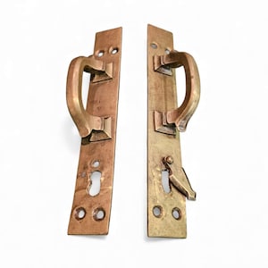 Puede incluir: Dos manijas de puerta antiguas de latón con placa trasera rectangular y manija curva. Una manija tiene cerradura y pestillo. Las manijas son de color latón cálido y están sobre un fondo blanco.