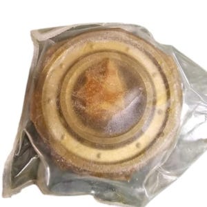 May include: A circular, metallic object in a light brown and gold colour scheme, encased in clear plastic. The object features concentric rings and small, evenly spaced holes around its perimeter. The design suggests a mechanical component.
