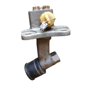 May include: A metallic gray mechanical component with a black rubber cap and a yellow plastic piece. The component has a series of bolts and a small metal tag. The item appears to be a part of a larger machine or engine.