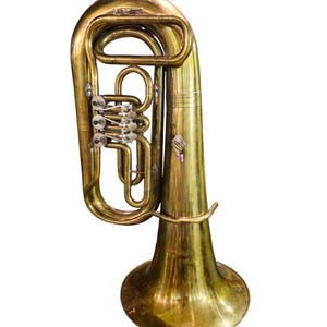 Puede incluir: Un eufonio de latón, un instrumento de viento metal de tono grave, se muestra sobre un fondo blanco. El instrumento tiene una campana, válvulas y tubos. El eufonio se utiliza a menudo en bandas de música y orquestas.