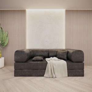 Puede incluir: Un sof&aacute; moderno de cuero marr&oacute;n oscuro con brazos y respaldo redondeados, con dos cojines cuadrados y un coj&iacute;n rectangular peque&ntilde;o. Una manta de color crema est&aacute; sobre el sof&aacute;. Una planta en maceta con hojas verdes grandes est&aacute; a la izquierda.