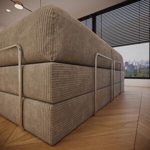 Puede incluir: Un gran sof&aacute; de pana beige con un dise&ntilde;o apilado. El sof&aacute; presenta una serie de cojines rectangulares y un marco de metal pulido. La habitaci&oacute;n tiene pisos de madera y una gran ventana con vista a la ciudad.