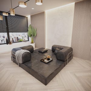 Puede incluir: Un sal&oacute;n moderno con un sof&aacute; modular de cuero negro. El sof&aacute; est&aacute; dispuesto en forma cuadrada, con un peque&ntilde;o otom&aacute;n cuadrado y una bandeja decorativa con flores. La habitaci&oacute;n tiene grandes ventanales y una planta.