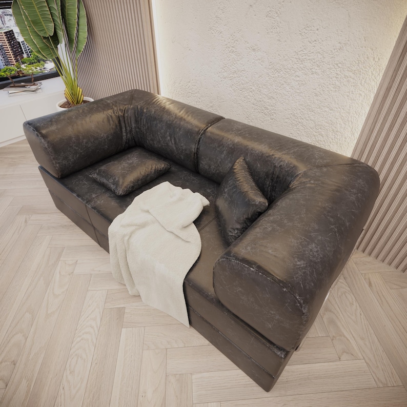 Puede incluir: Un sof&aacute; seccional de cuero gris oscuro con dos cojines a juego y una manta de color crema. El sof&aacute; tiene un aspecto texturizado y es de estilo moderno. La habitaci&oacute;n tiene piso de madera clara.