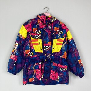 May include: A colorful vintage ski jacket with a vibrant geometric pattern. The jacket features a mix of purple, blue, yellow, and pink hues, with checkered and abstract designs. It has multiple pockets, a hood, and a drawstring waist. The jacket is hanging on a hanger.
