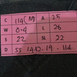 Puede incluir: Primer plano de una prenda verde oscuro con una etiqueta rosa. La etiqueta muestra las medidas: C 114, W 0,4, S 22, A 25, L 26, SL 22. La prenda tiene un patr&oacute;n de rayas en la parte superior.