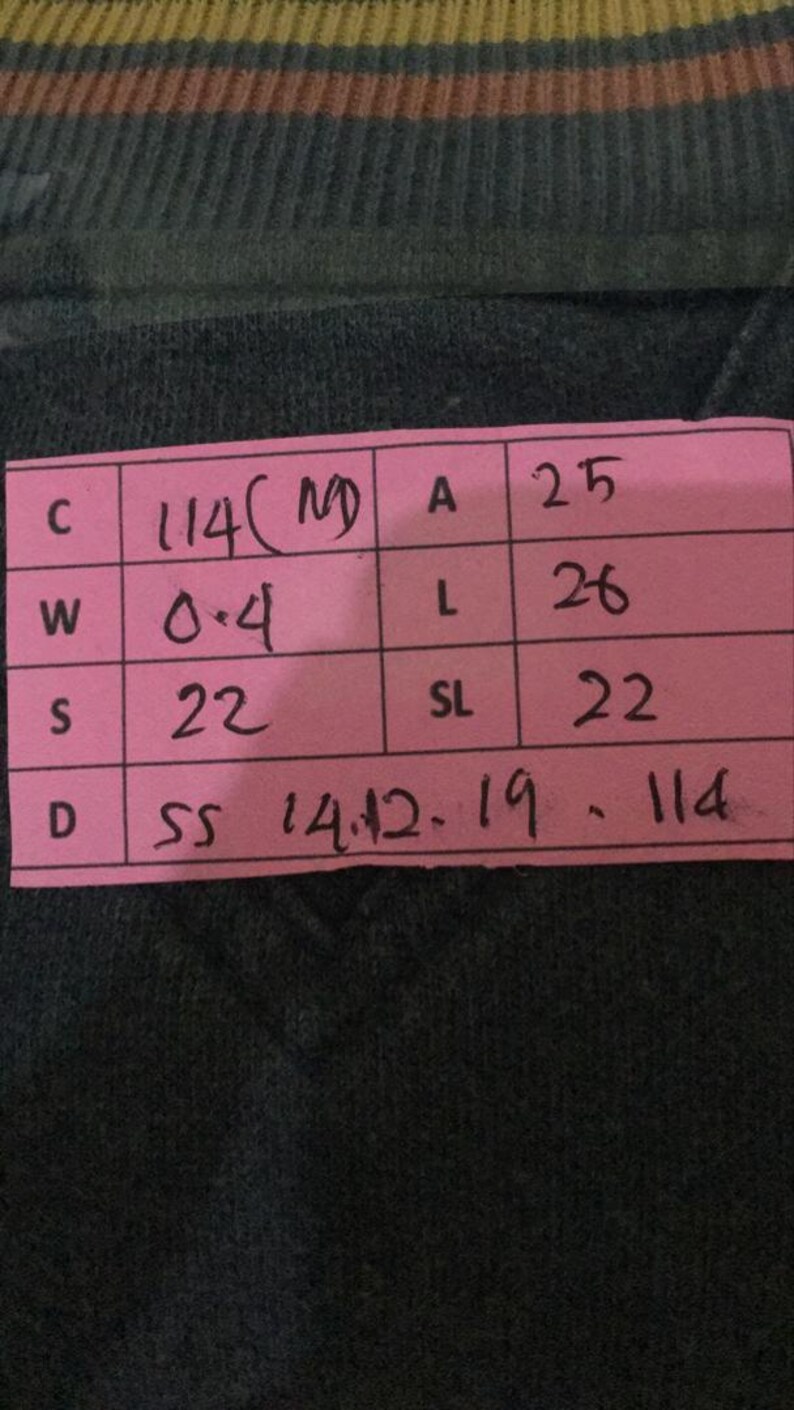 Puede incluir: Primer plano de una prenda verde oscuro con una etiqueta rosa. La etiqueta muestra las medidas: C 114, W 0,4, S 22, A 25, L 26, SL 22. La prenda tiene un patr&oacute;n de rayas en la parte superior.
