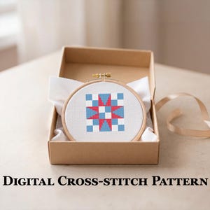 May include: A cross-stitch pattern in a wooden hoop, featuring a geometric design with red, white, and blue squares and a star. The hoop is presented in a brown cardboard box with white fabric. The text "DIGITAL CROSS-STITCH PATTERN" is at the bottom.