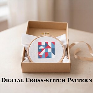 May include: A cross-stitch pattern in a wooden hoop, featuring a geometric design in red, white, and blue, is displayed inside a cardboard box. The text "DIGITAL CROSS-STITCH PATTERN" is visible at the bottom of the image.