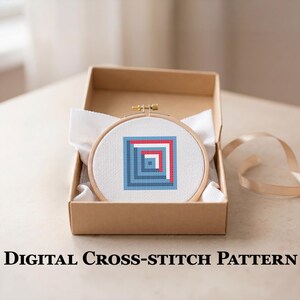 May include: A cross-stitch design in a wooden hoop, with a geometric pattern of blue and red squares, is displayed in a brown cardboard box. The text "DIGITAL CROSS-STITCH PATTERN" is below the box. White fabric and a ribbon are also visible.