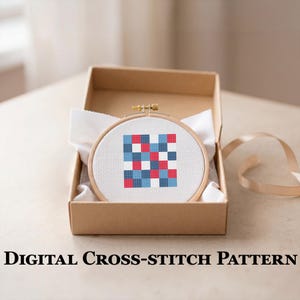Può includere: Un motivo a punto croce in un telaio di legno, con un design geometrico di quadrati rossi, bianchi e blu. Il telaio è presentato in una scatola di cartone marrone con tessuto bianco. Il testo "DIGITAL CROSS-STITCH PATTERN" è visualizzato sotto.