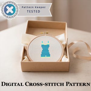 May include: A round wooden embroidery hoop containing white Aida fabric with a cross-stitch design of a blue and yellow striped one-piece swimsuit, presented in a cardboard box with a Pattern Keeper Tested logo and digital cross-stitch pattern text.