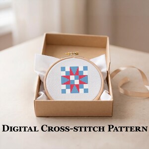 May include: A cross-stitch design in a wooden hoop, with a geometric pattern of red, white, and blue squares and a star. The hoop is displayed in a brown cardboard box with white fabric. The text "DIGITAL CROSS-STITCH PATTERN" is at the bottom.