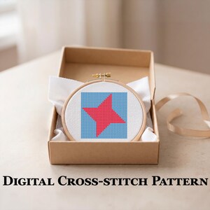 May include: A round wooden embroidery hoop containing white Aida fabric with a cross-stitch design of a red four-pointed star on a light blue square background, presented inside an open cardboard box. The text reads Digital Cross-Stitch Pattern.