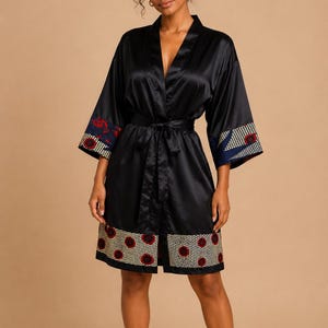 May include: Black satin robe with patterned trim. The robe features a V-neck, a matching tie belt, and patterned cuffs and hem. The trim has a design of red circles on a yellow background, with blue and white accents.