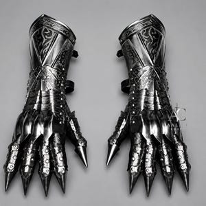 Puede incluir: Un par de guanteletes de metal oscuro con intrincados patrones de volutas grabados en los pu&ntilde;os y placas de dedos articuladas que terminan en puntas afiladas. La superficie met&aacute;lica tiene un acabado pulido con remaches visibles y el texto AC AALAM CRAFTS.