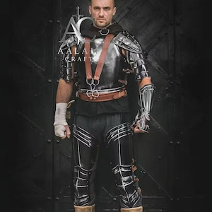 Puede incluir: Un conjunto de armadura de metal negro que incluye una coraza pulida, hombreras segmentadas, brazales y grebas. La armadura se asegura con correas y hebillas de cuero marrón. El logotipo AALAM CRAFT es visible en el área del pecho.