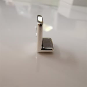 May include: A polished, silver-toned, L-shaped metal component. It features a rectangular base and a vertical, gently curved section. The surface reflects light, producing highlights and shadows. The object appears to be a small, industrial part.
