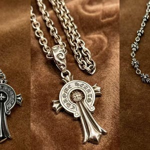 May include: Three silver necklaces with cross pendants. Each pendant has a keyhole design with intricate detailing. The chains vary in style, with one featuring a floral pattern. The jewelry is displayed on a brown surface.