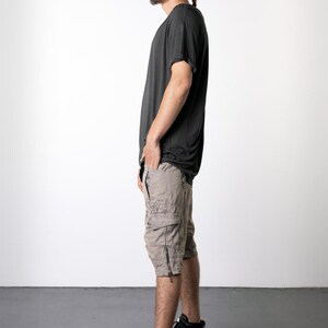 May include: Dark gray t-shirt and tan cargo shorts with multiple pockets and zippers. The person is wearing black high-top sneakers with white soles. The outfit is casual and suitable for everyday wear.