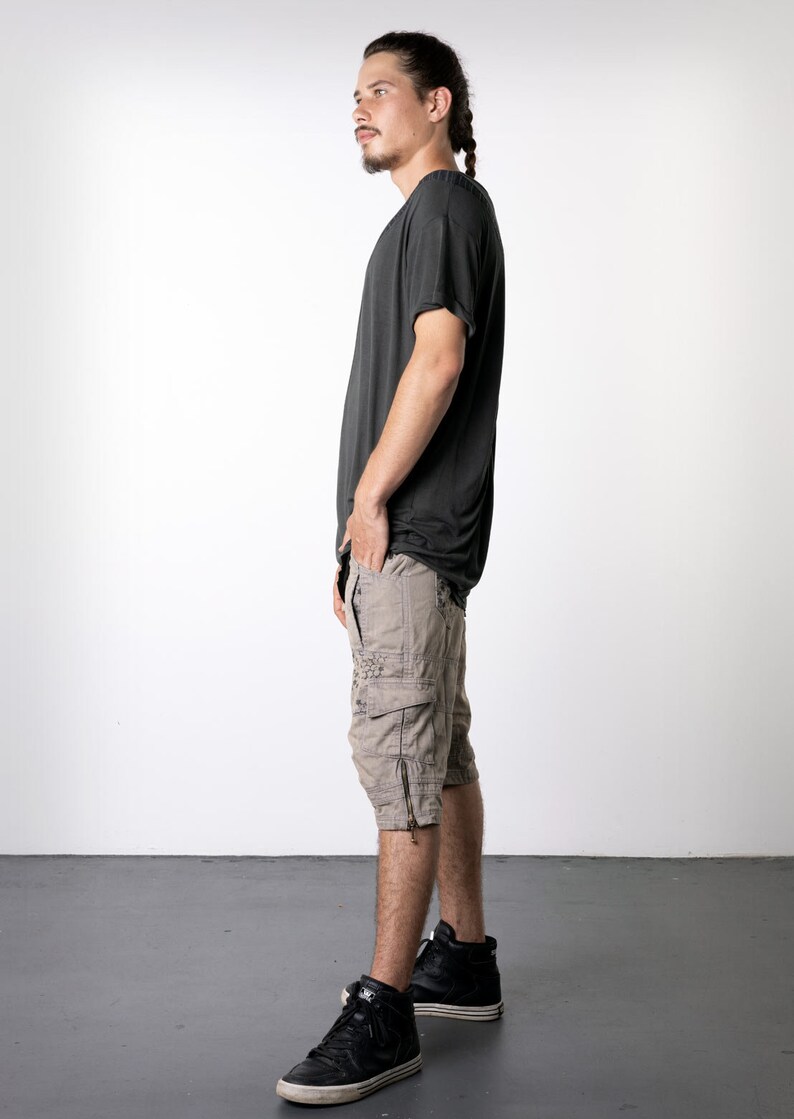 May include: Dark gray t-shirt and tan cargo shorts with multiple pockets and zippers. The person is wearing black high-top sneakers with white soles. The outfit is casual and suitable for everyday wear.