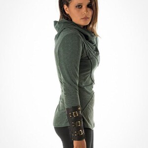 May include: A green long-sleeved shirt with a cowl neck and a brown leather cuff with metal buckles.