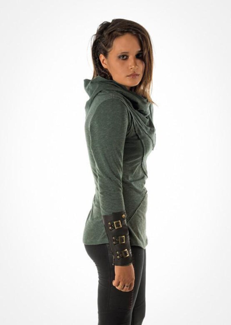 May include: A green long-sleeved shirt with a cowl neck and a brown leather cuff with metal buckles.