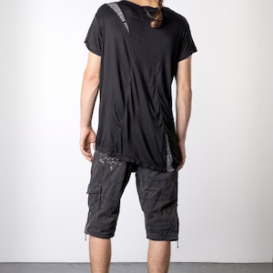 May include: Black t-shirt with a unique design, paired with dark gray cargo shorts. The shorts feature multiple pockets and a distressed look. The outfit is completed with black high-top sneakers.