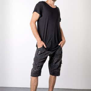 May include: Black t-shirt with an asymmetrical design and black cargo shorts. The shorts have multiple pockets and a distressed pattern. The person is wearing black high-top sneakers.
