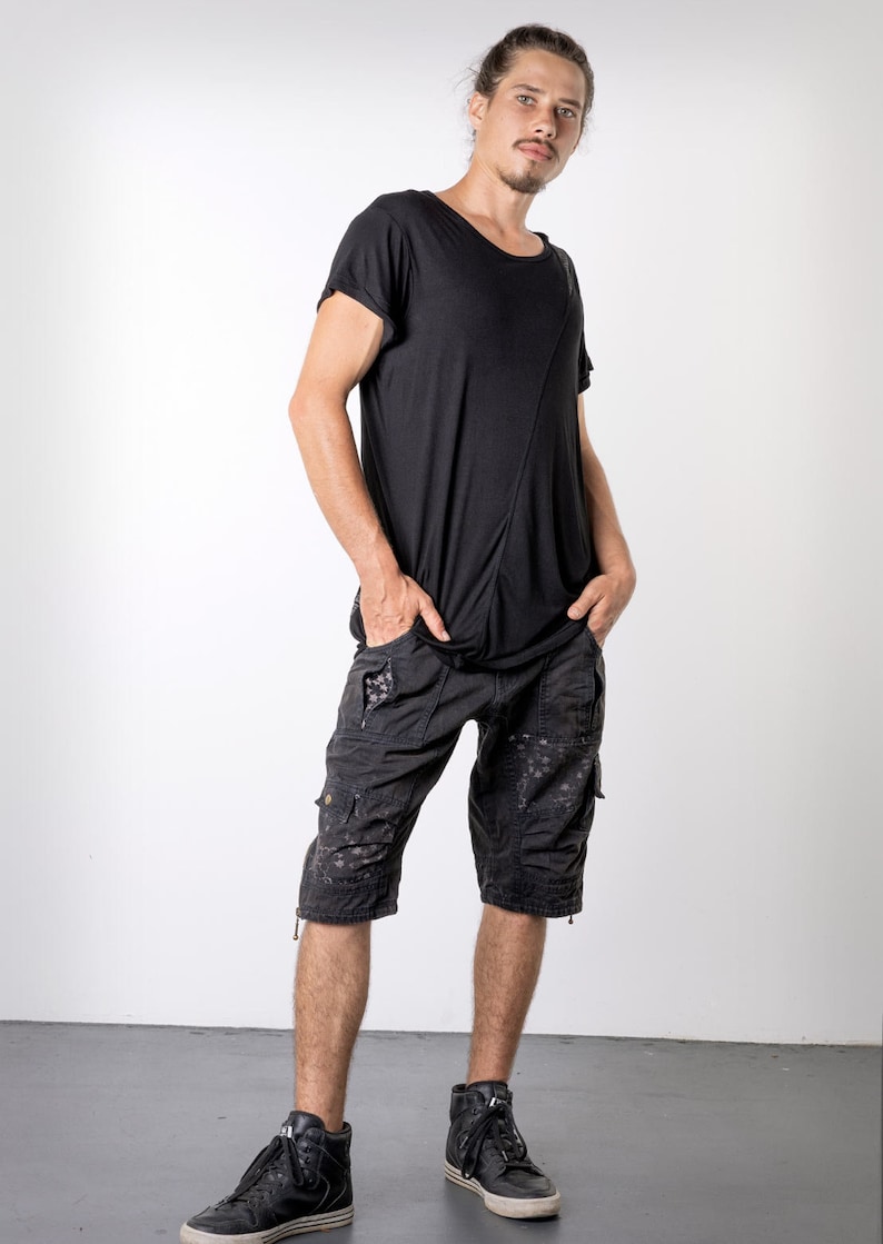 May include: Black t-shirt with an asymmetrical design and black cargo shorts. The shorts have multiple pockets and a distressed pattern. The person is wearing black high-top sneakers.
