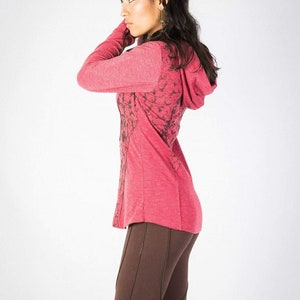 May include: A red hooded sweatshirt with a black and white floral pattern. The sweatshirt is worn by a person with long dark hair. The person is wearing brown pants.