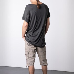 May include: Dark gray t-shirt with a unique design, paired with tan cargo shorts. The shorts feature multiple pockets and decorative stitching. Black high-top sneakers complete the outfit, offering a modern, casual look. The model has a braided hairstyle.