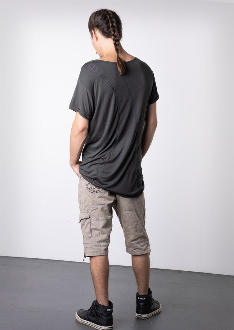 May include: Dark gray t-shirt with a unique design, paired with tan cargo shorts. The shorts feature multiple pockets and decorative stitching. Black high-top sneakers complete the outfit, offering a modern, casual look. The model has a braided hairstyle.