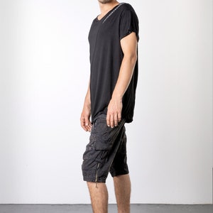 May include: Black t-shirt with a V-neck and short sleeves. The shirt is paired with black cargo shorts featuring multiple pockets and a zipper detail. The outfit is completed with black high-top sneakers. The model is standing in front of a white background.