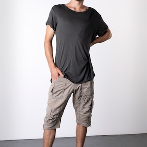 May include: A dark gray short-sleeved t-shirt with a diagonal seam detail, paired with khaki cargo shorts featuring decorative embellishments. The outfit is completed with black high-top sneakers.