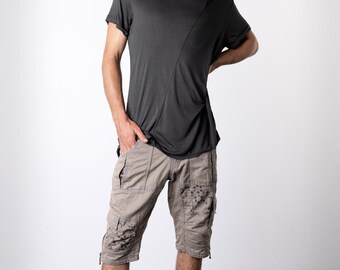 Könnte beinhalten: Ein dunkelgraues kurzärmeliges T-Shirt mit diagonalen Nahtdetails, kombiniert mit khakifarbenen Cargoshorts mit dekorativen Verzierungen. Abgerundet wird das Outfit durch schwarze High-Top-Sneaker.